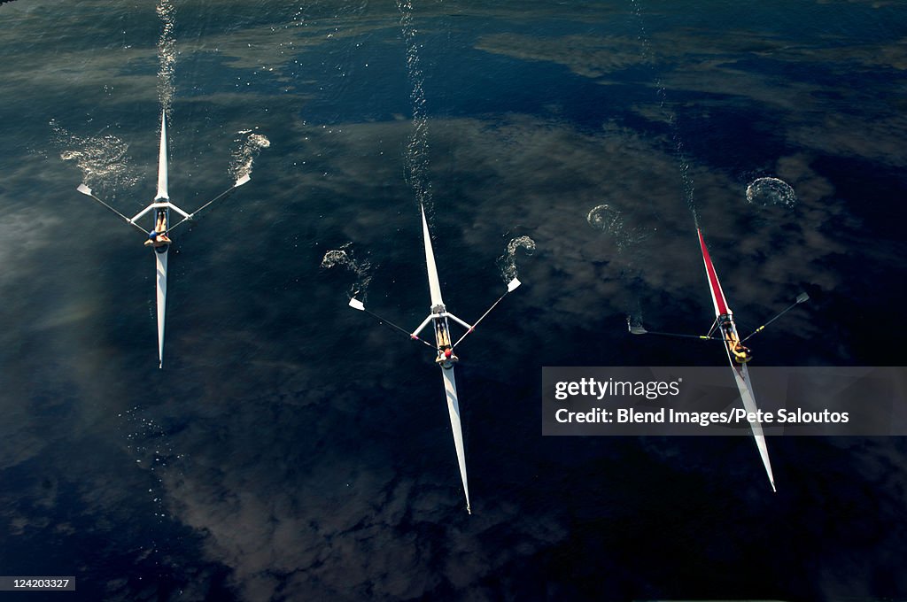 People rowing sculling boats on river