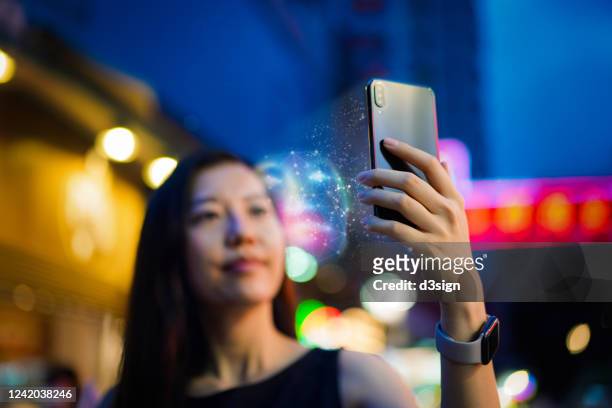 young asian woman using face recognition software via smartphone, in front of colourful neon signboards in busy downtown city street at night. biometric verification and artificial intelligence concept - digital identity stockfoto's en -beelden
