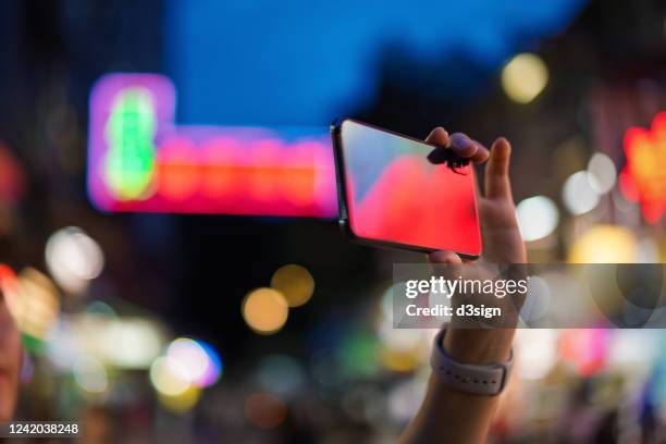 cropped shot of young asian woman photographing the vitality of city night scene with smartphone, in front of colourful neon signboards in busy downtown city street - asien metropole nachtleben stock-fotos und bilder