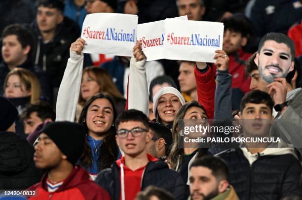 Fans of Nacional hold a mask with an image of Uruguayan football star Luis Suarez and placards reading #SuárezANacional as part of a campaign to try...