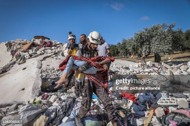 July 2022, Syria, Idlib: A member of the White Helmets carries the body of a girl who was killed as a result of a Russian air strike targeted a house...