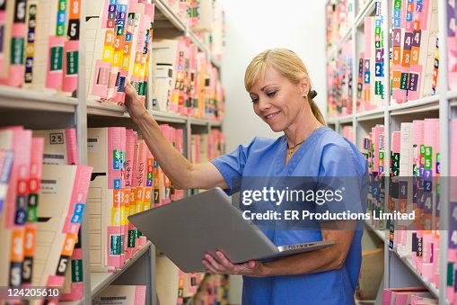 Caucasian doctor searching for medical record in file room with laptop Caucasian doctor searching for medical record in file room with laptop