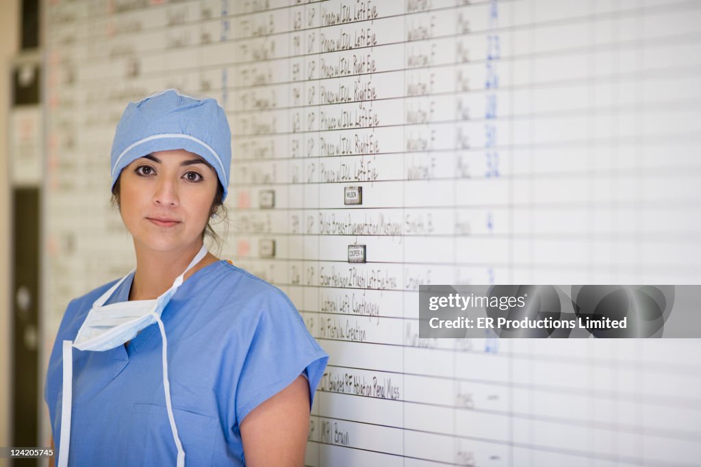 Hispanic doctor standing by schedule whiteboard in hospital