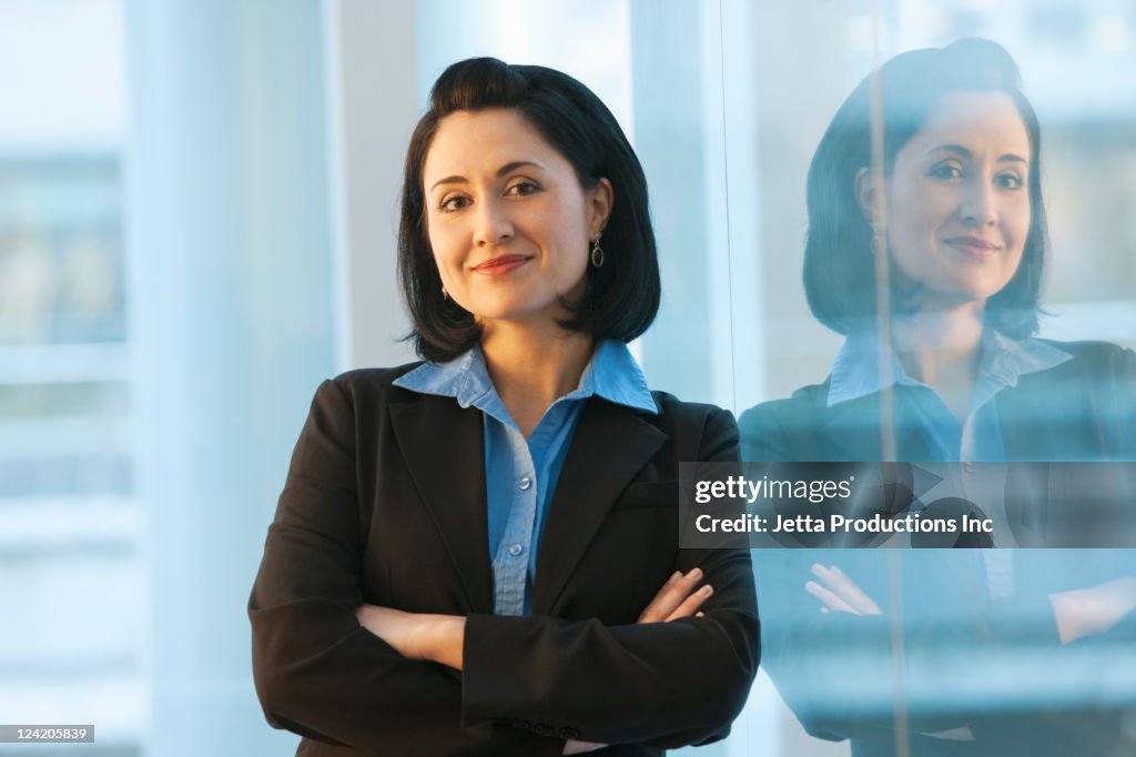 Mixed race businesswoman leaning on wall with arms crossed