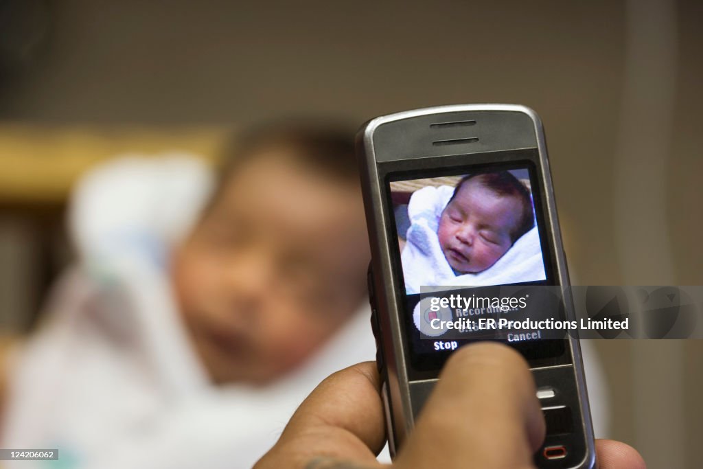 Hispanic mother taking camera phone picture of newborn baby boy