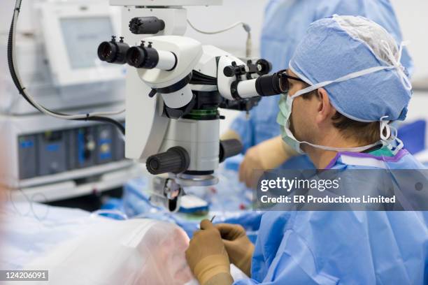 doctors performing microsurgery in operating room - microchirurgie stockfoto's en -beelden