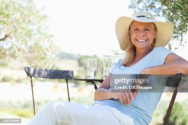 portrait de femme d'âge mûr heureuse assis sur une chaise - chapeau de soleil photos et images de collection