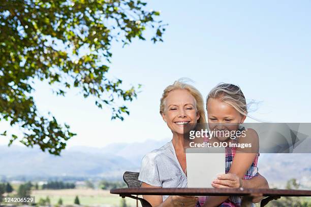 joyeuse fille avec sa grand-mère de lecture e-reader sur la pelouse - fille lire gazon photos et images de collection