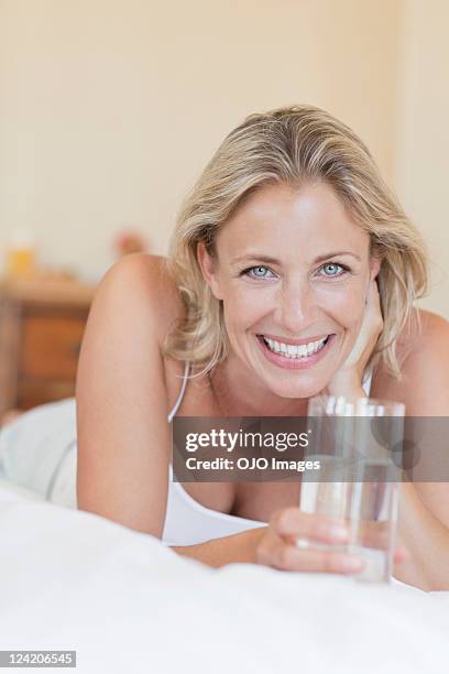 portrait of beautiful mature woman lying in bed with a glass of water - mature woman in water stock pictures, royalty-free photos & images