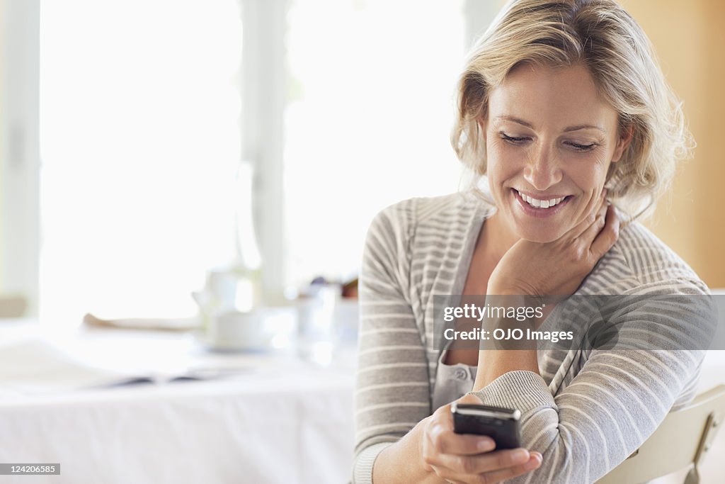 Happy mature woman using cell phone at home