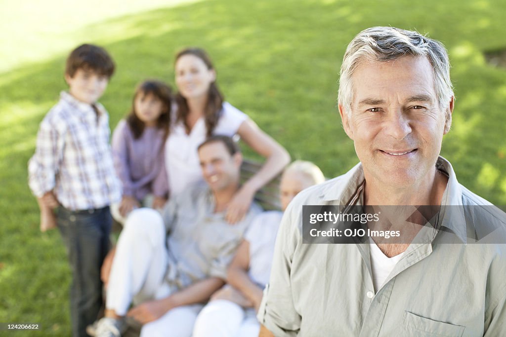 Happy senior man with his family in the background in park