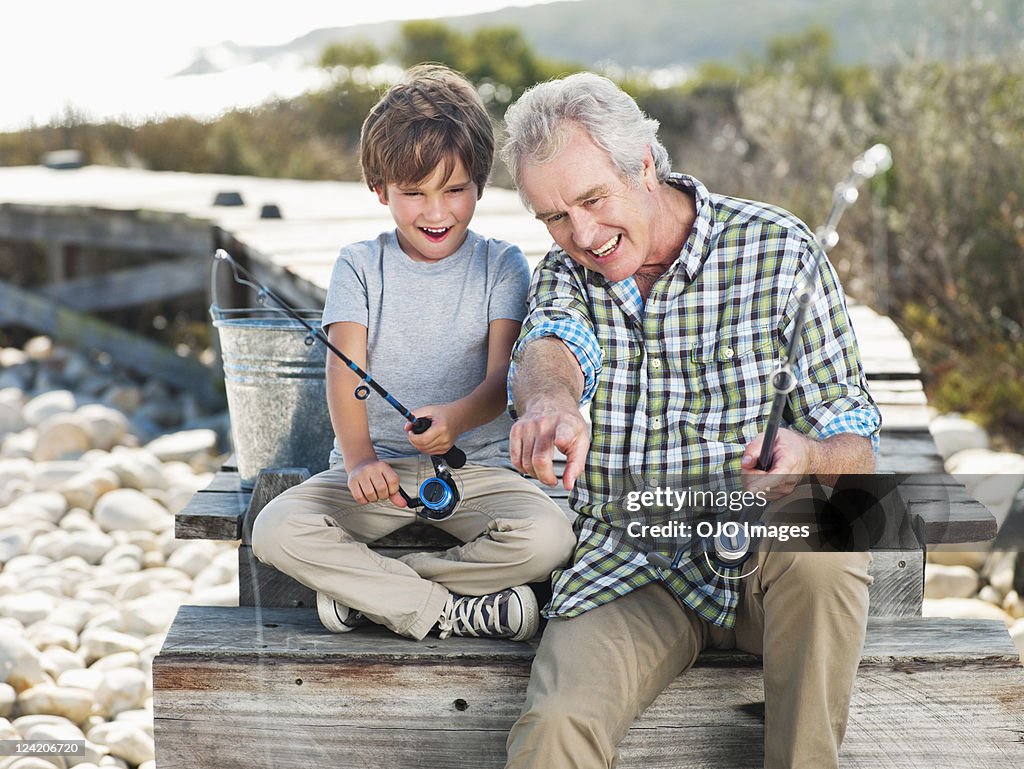 Cheerful senior man fishing with boy on pier