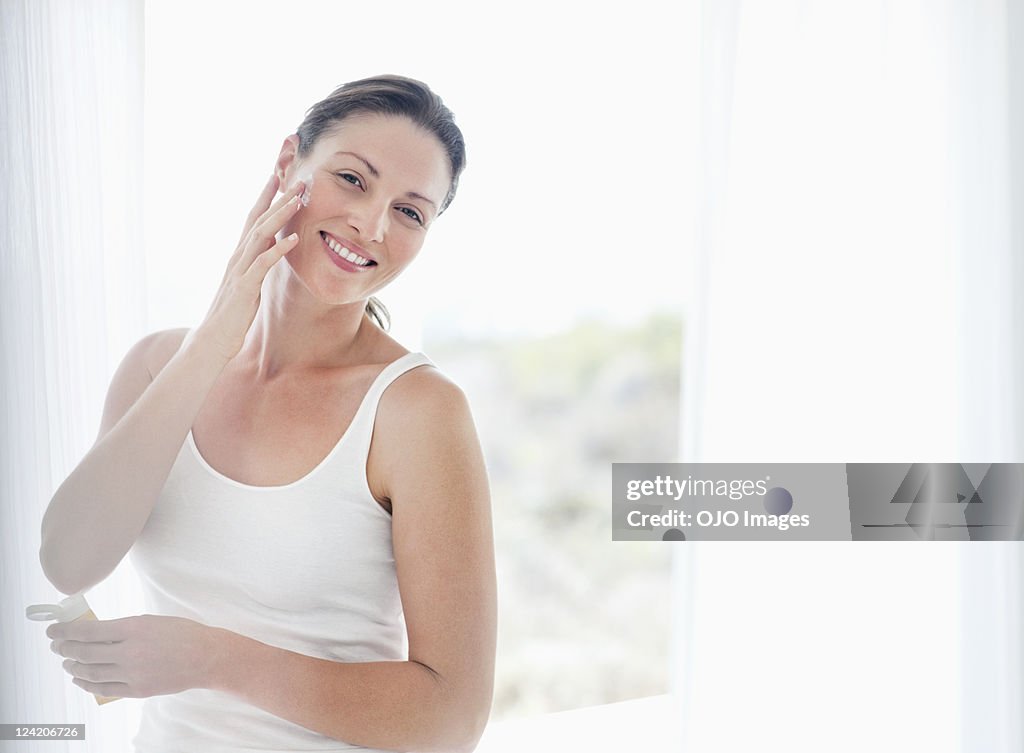 Beautiful mid adult woman applying moisturizer on cheek