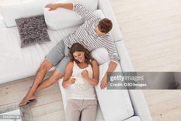 high angle view of young couple reading book in sofa - young couple on couch stock pictures, royalty-free photos & images