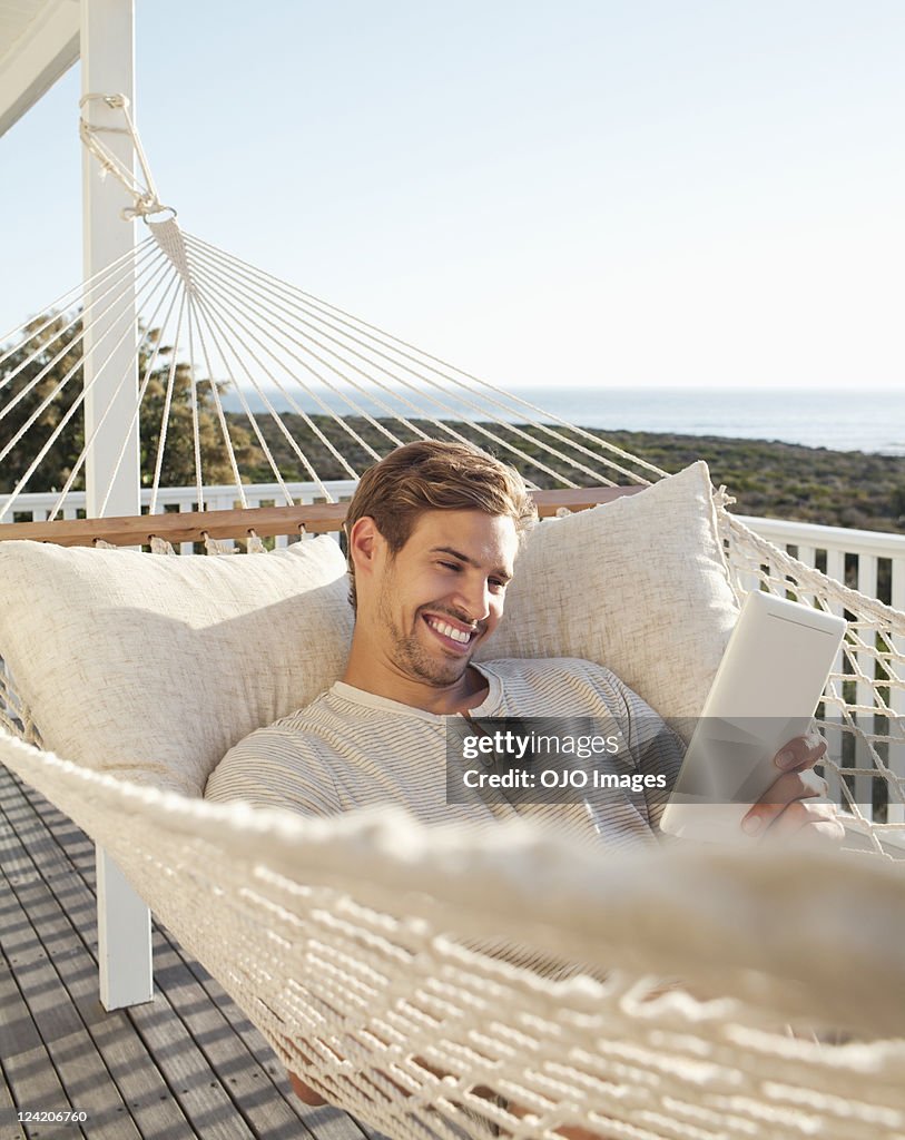 Happy young man reading electronic book in hammock