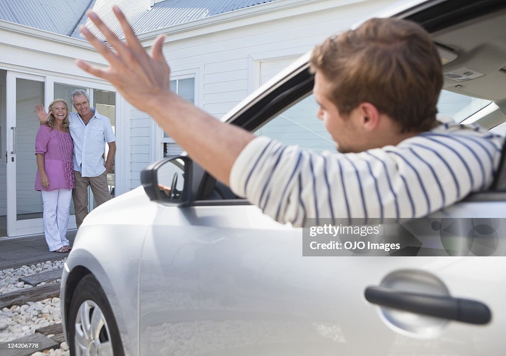 Young man in car waving goodbye to parents