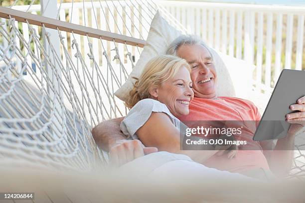 happy couple looking at electronic book in hammock - baby boomer stock pictures, royalty-free photos & images