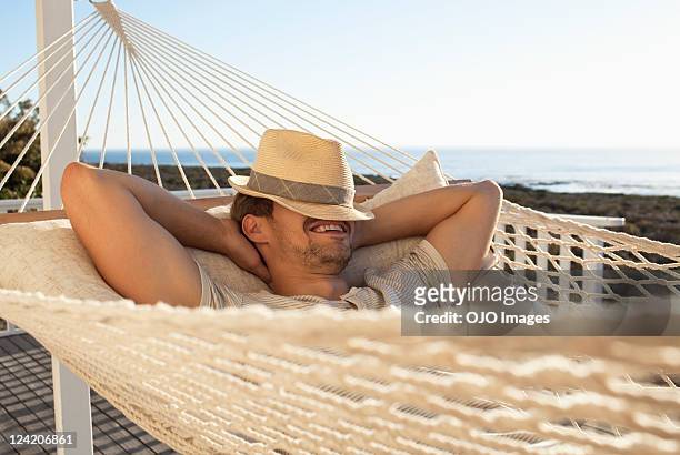 cheerful young man smiling in hammock with his face covered by a hat - hammock 個照片及圖片檔