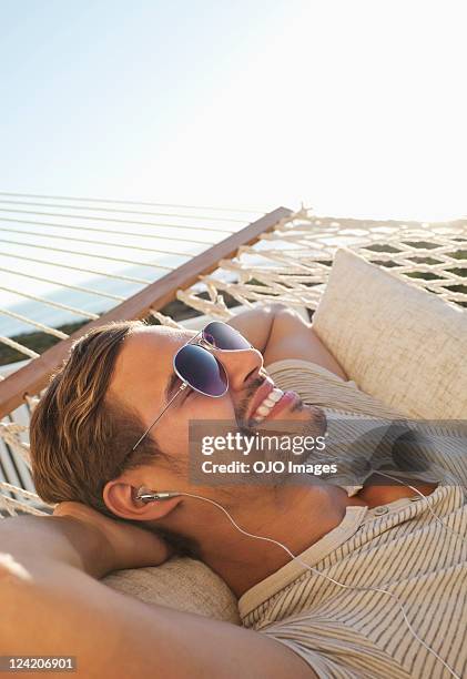 happy young man relaxing in hammock and listening to music - young man listening music and relaxing in hammock stock pictures, royalty-free photos & images