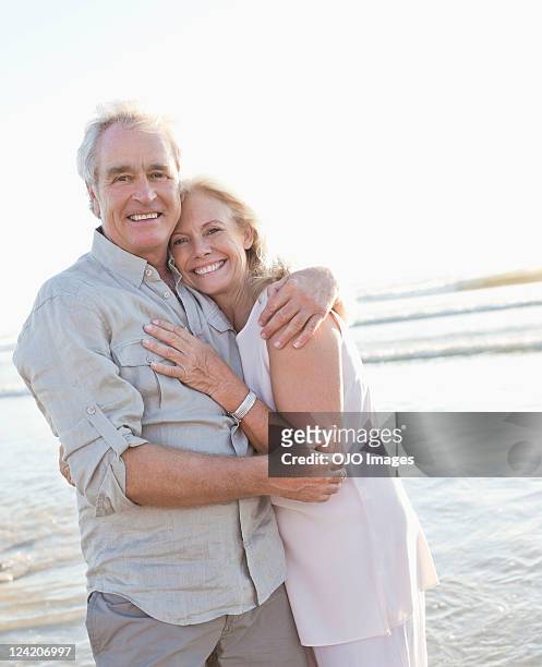 portrait of a cheerful couple hugging on beach - baby boomer stock pictures, royalty-free photos & images