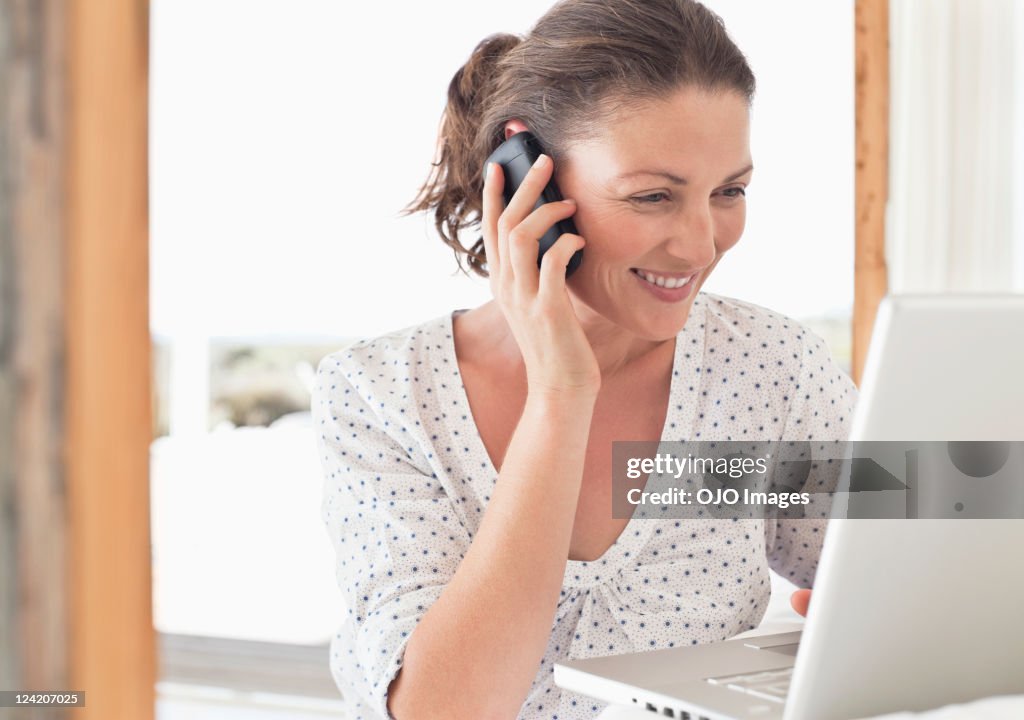 Beautiful mid adult woman on phone smiling and using laptop