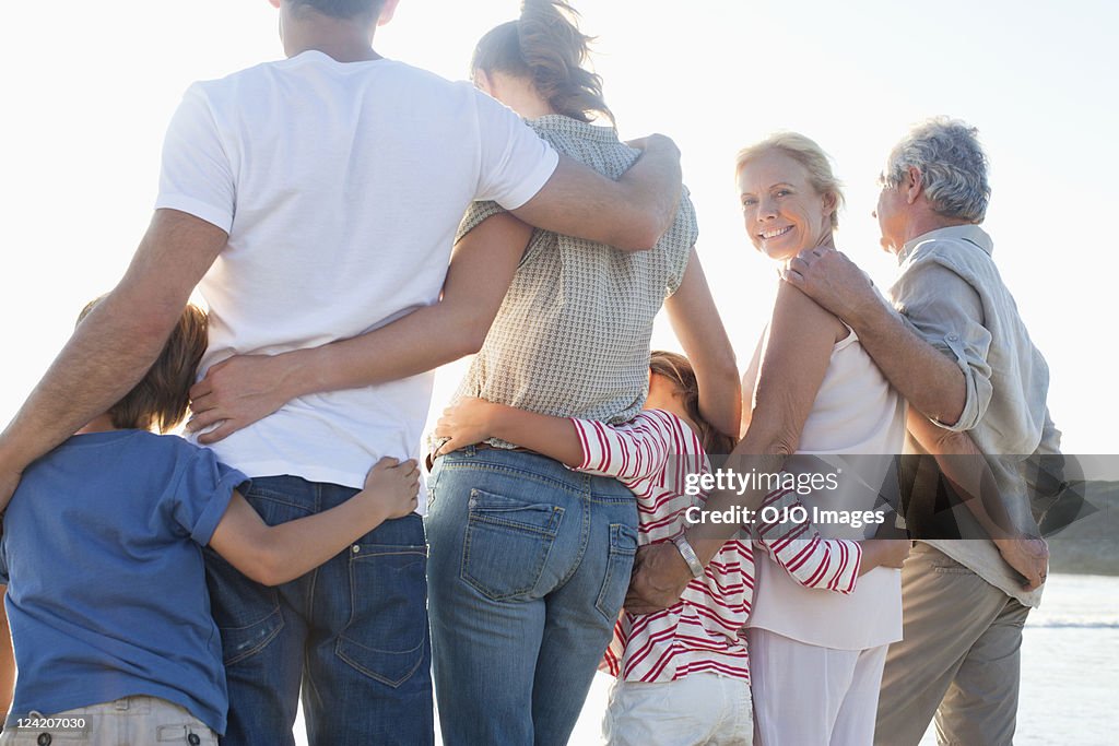 Vista traseira de família geração três na praia, a desfrutar de Pé