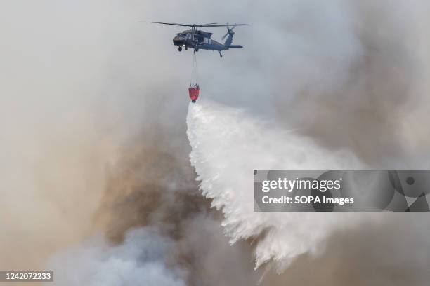 Slovakian Sikorsky UH-60 Black Hawk helicopter carrying a Bambi bucket for extinguishing fires drops water on a large wildfire that burns near the...