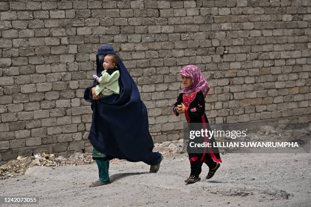 Burqa-clad woman walks with children on the outskirts of Kandahar city on July 23, 2022.