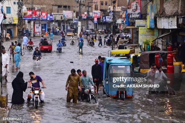 Commuters make their way through a flooded street during monsoon rainfall in Hyderabad on July 24, 2022.