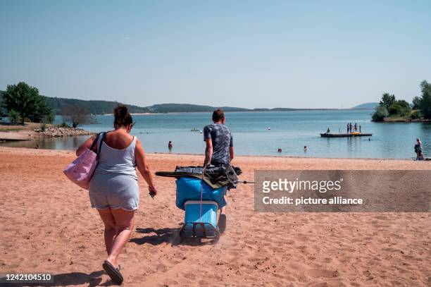 July 2022, Bavaria, Pleinfeld: Bathers go to the bathing beach. At the bathing beach Ramsberg at the Großer Brombachsee some bathers can already be...