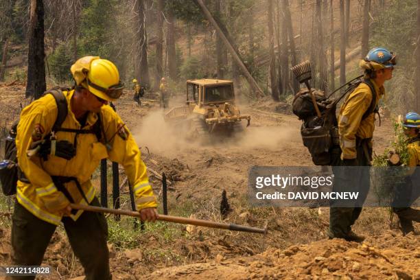 Bulldozer passes firefighters cutting vegetation to broaden a fireline at the Oak Fire near Mariposa, California, on July 25, 2022. Firefighters were...