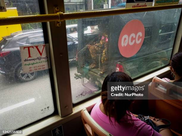 Two women look out the window of a bus as armed soldiers patrol a main street in Yangon, Myanmar on July 26, 2022.