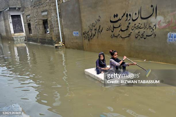 Girls use a temporary raft across a flooded street in a residential area after heavy monsoon rains in Karachi on July 26, 2022. A weather emergency...
