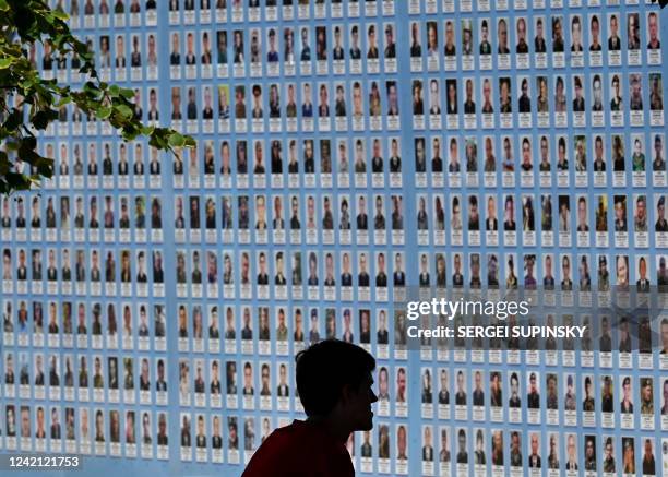 Man sits looking at a memorial wall displaying images of Ukrainian Servicemen and women killed since Russia invaded Ukraine in February, in the...