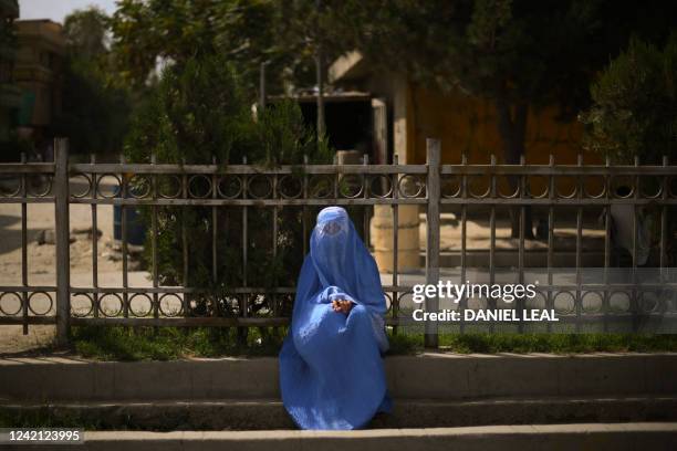 Burqa-clad woman sits on the side of the road in Kabul on July 26, 2022.