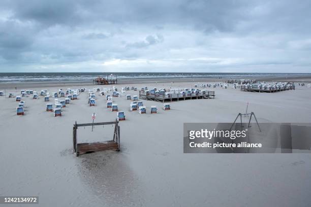 July 2022, Schleswig-Holstein, St. Peter Odring: Sand drifts can be seen between beach chairs on the beach of St. Peter Ording in windy weather. With...