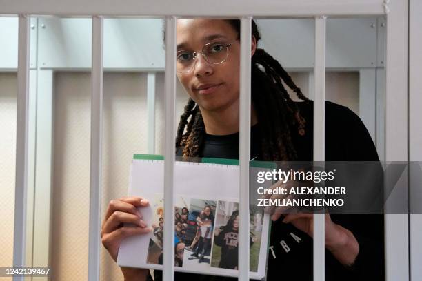 Basketball superstar Brittney Griner holds photographs standing inside a defendants' cage before a hearing at the Khimki Court, outside Moscow on...