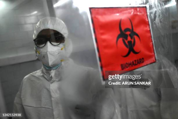 Technicians wearing personal protective equipment suits stand behind a biohazard sign inside a molecular laboratory facility set up to test for the...