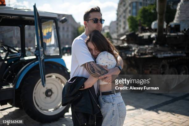 Couple hugs by the burnt Russian military vehicles that are displayed on St. Michaels Square on July 28, 2022 in Kyiv, Ukraine.