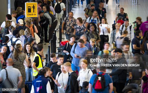 Passengers queue to check-in for flights at the Schiphol Airport on 29 July 2022. - Schiphol has been struggling with a shortage of security guards...