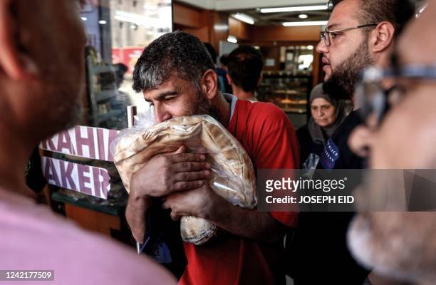 Man walks out of a bakery clutching a bag of subsidised flatbread, as others continue to wait in a queue, in the Lebanese capital Beirut on July 29...
