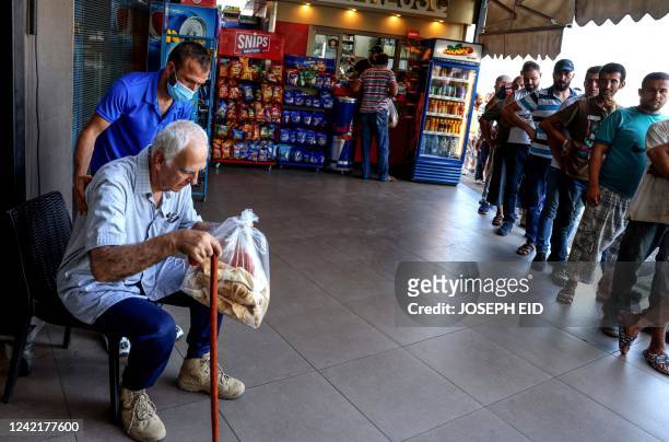 An elderly man rests outside a bakery after buying a bag of subsidised flatbread, as others continue to wait in a queue, in the Lebanese capital...
