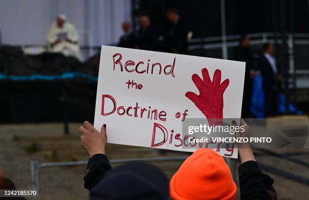 Person holds a protest sign reading "Recind the Doctrine of Discovery" as Pope Francis speaks on stage at Nakasuk Elementary School Square in...