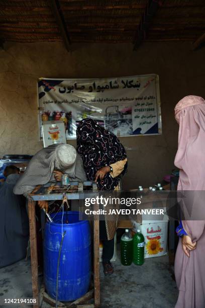 Afghan burqa-clad women workers fill the machine at a shampoo and soap factory in Kandahar on July 30, 2022.