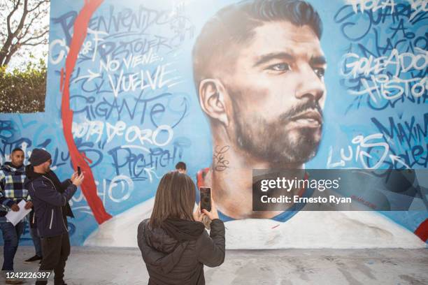 Fans pose in front of a mural with the face of Luis Suarez outside the Parque Central Stadium prior to the unveiling of Uruguayan football player...