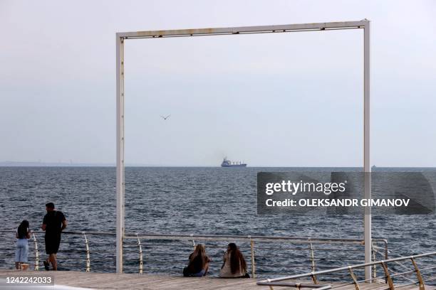 Members of the public sit on a quay as bulk carrier M/V Razoni, carrying a cargo of 26,000 tonnes of corn, leaves Ukraines port of Odessa, en route...