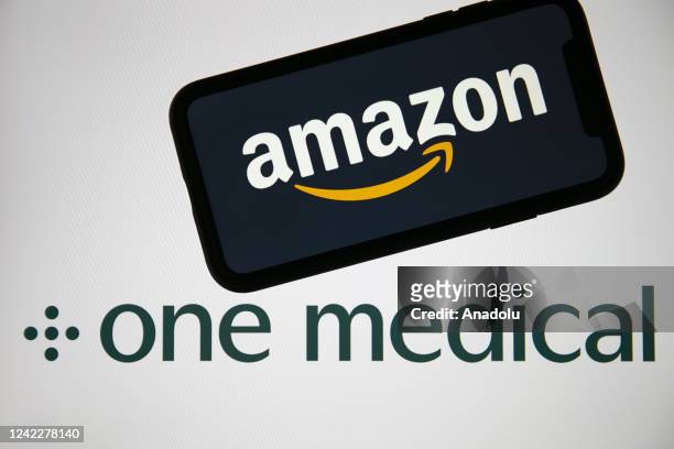 In this photo illustration, logo of "Amazon Inc" is displayed on a mobile phone screen in front of a computer screen displaying "One Medical" in...