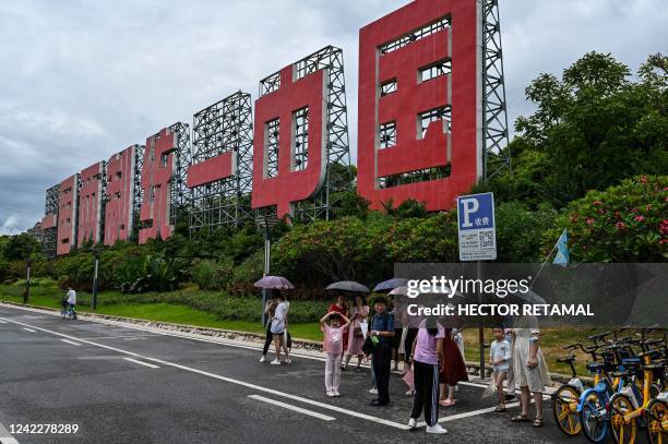 People wait for a bus on a street next to a sign that reads in Chinese "one country two systems to unify China", in Xiamen, Fujian province on August...