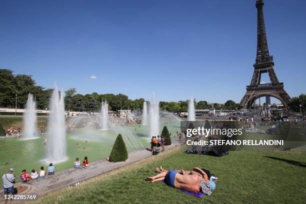 Couple sunbathes as others cool off at the Trocadero fountain, with the Eiffel Tower in background, on a sunny summer afternoon in Paris, on August...