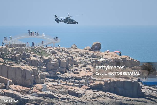 Tourists look on as a Chinese military helicopter flies past Pingtan island, one of mainland China's closest point from Taiwan, in Fujian province on...